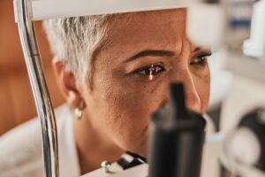 A woman sits in an optometrist's office with her eye in a medical machine.