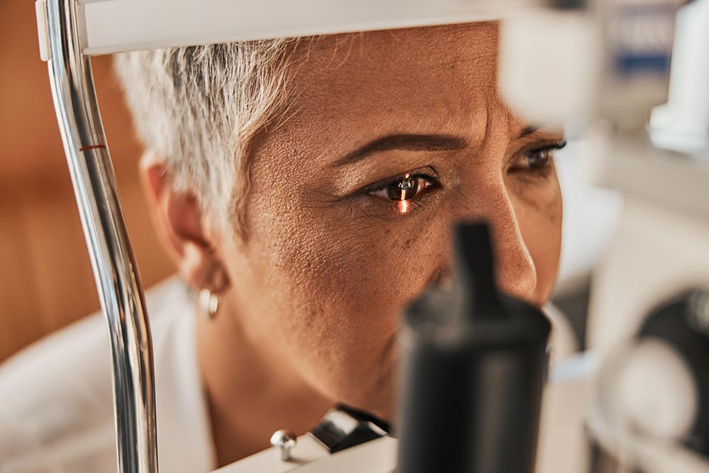 A woman sits in an optometrist's office with her eye in a medical machine.